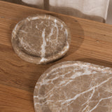 Two oval stone trays with a beige and white marble pattern, one small round tray and one larger elongated tray, displayed on a wooden tabletop.