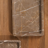 Two rectangular marble trays with rounded corners, one large and one small, both featuring brown and beige veining, arranged on a wooden surface.